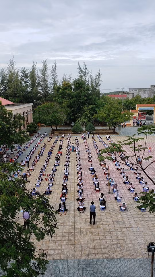 Theo như loạt ảnh chia sẻ trên MXH, các bạn học sinh ngồi bệt xuống đất, cách nhau mỗi người từ 1,5 đến 2 mét tạo thành các hàng dài ngồi dọc khắp sân để làm bài kiểm tra tập trung.