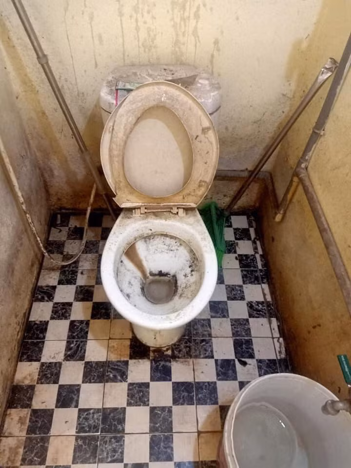 Bồn cầu bám đầy bụi đen bẩn thỉu, nắp bồn cầu vỡ nát, các bức tường xung quanh bụi bẩn đóng thành từng mảng.