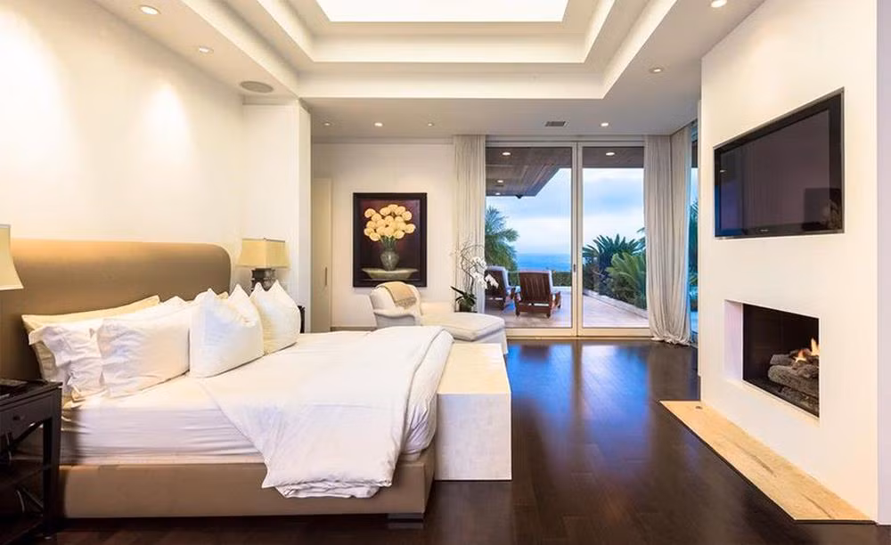 Phòng ngủ chính rộng lớn trông đơn giản nhưng lại sang trọng với sàn gỗ, lò sưởi, chiếc gường khổng lồ. Những tấm kính trượt dẫn ra ngoài ban công để ngắm cảnh, nơi Simon Cowell có những phút giây thư thái cho riêng mình.