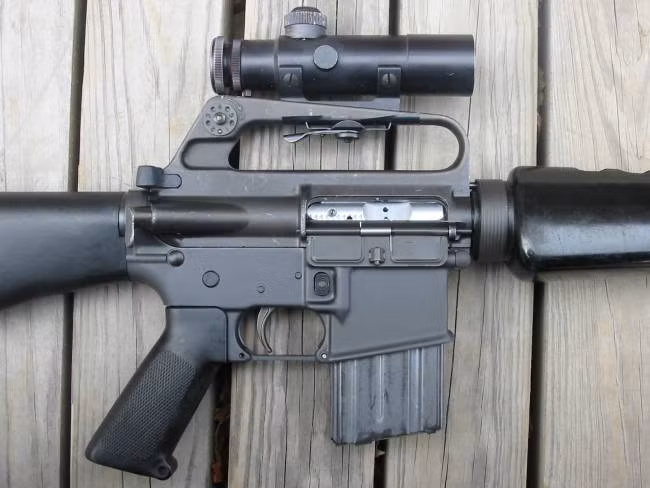 Điểm gây khó chịu đầu tiên và tạo ra không ít tai tiếng cho khẩu AR-15 chính là cái nắp che bụi ở khóa nòng. Nắp che hộp khóa nòng của nó phải luôn luôn mở khi súng ở trạng thái sẵn sàng chiến đấu và có tác dụng là nơi để đẩy vỏ đạn ra. Nguồn ảnh: Guns.
