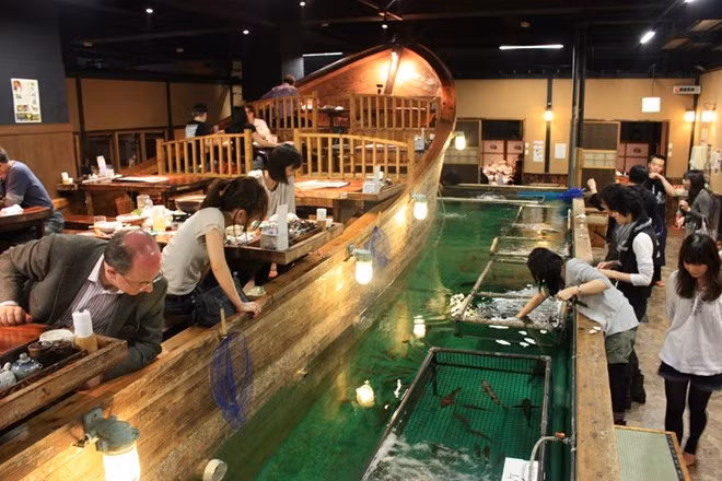 Tự tìm nguyên liệu cho bữa ăn: Ở nhà hàng Zauo, Tokyo, nếu muốn có đồ ăn, trước hết bạn phải tự bắt cá bằng cách sử dụng cần câu và vợt. Bạn không thể thả lại con đã bắt xuống bể. Mỗi khi cá cắn câu, nhân viên nhà hàng sẽ gõ trống ăn mừng. Bàn ăn được bày trên một thuyền gỗ lớn nhìn ra chỗ các thực khách đang câu cá. Ảnh: Blog.zingarate.com.