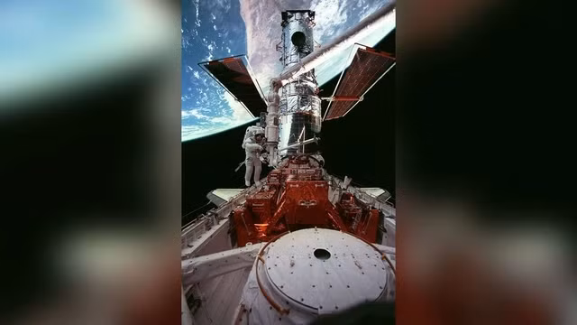 Phi hành gia Steven L. Smith di chuyển dọc theo kính viễn vọng không gian Hubble khi cập bến khoang chở hàng của tàu con thoi Discovery.