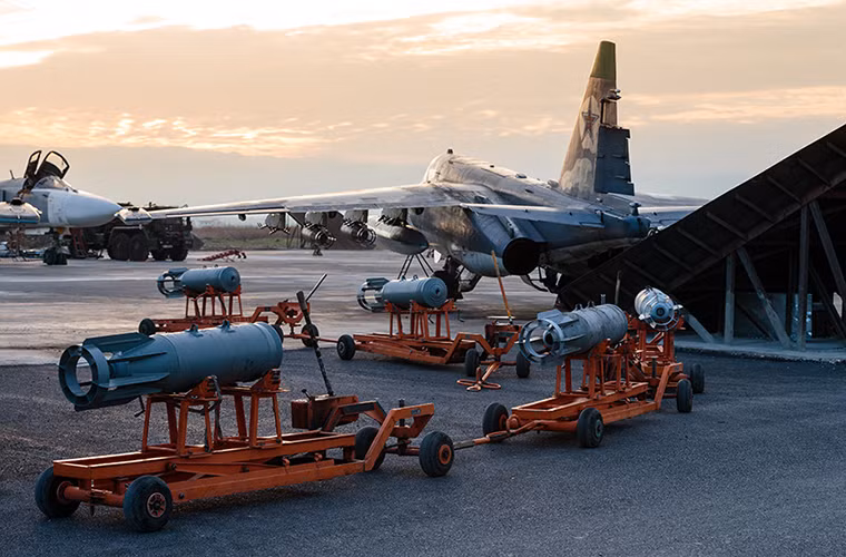 Su-25 được sử dụng cho hầu như mọi nhiệm vụ không kích tại Syria một phần là nhờ khả năng tấn công mặt đất tuyệt vời của nó. Trong ảnh là một hàng dài bom OFAB-250-270 đợi được lắp lên một chiếc Su-25.