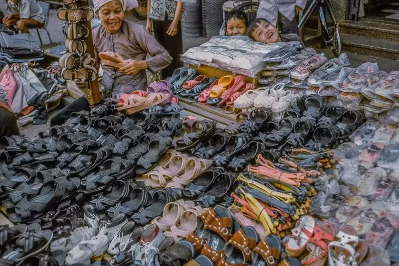 Người bán giày và hai đứa trẻ đang tươi cười khi thấy máy ảnh.