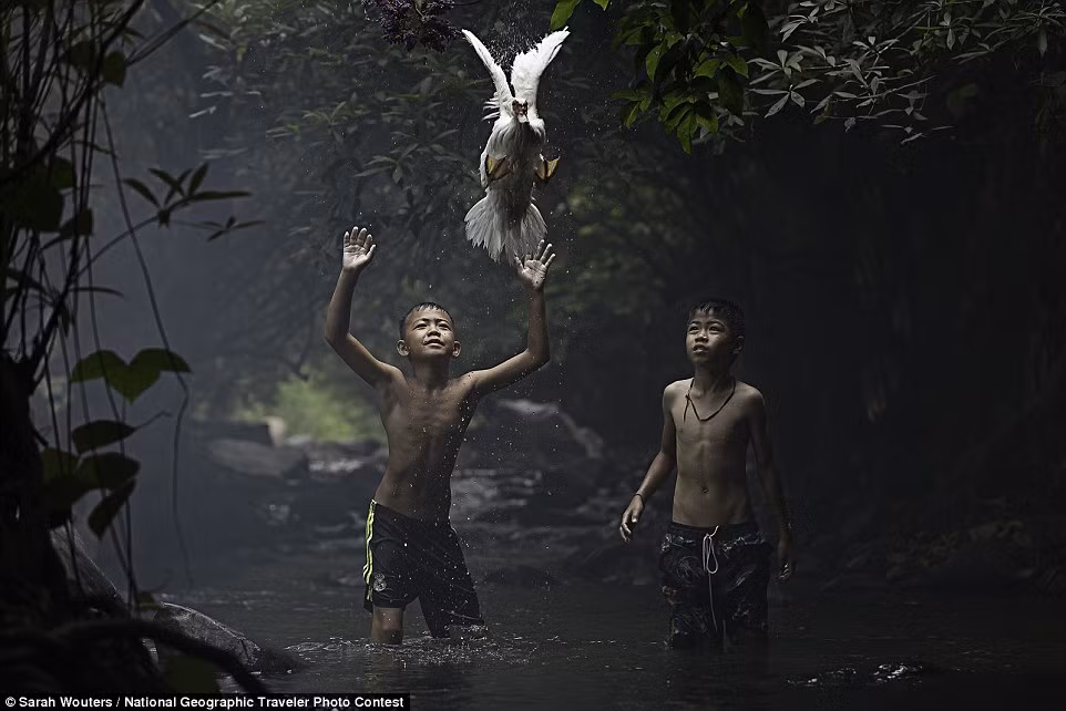 Hai cậu bé cố gắng bắt vịt dưới một dòng suối ở tỉnh Nong Khai, Thái Lan.