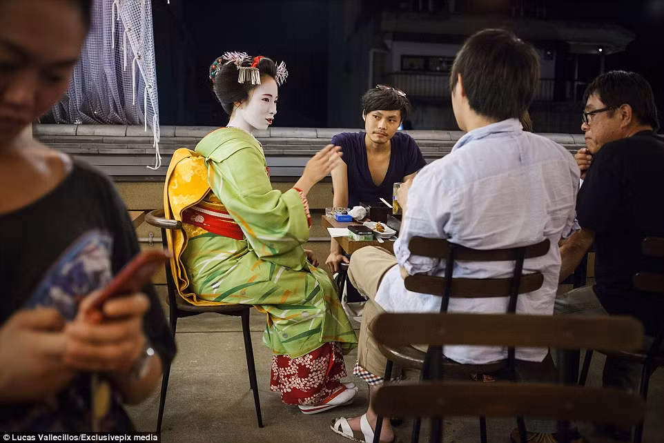 Nhóm khách hàng chăm chú lắng nghe và quan sát một geisha học việc đang trổ tài trà đạo.
