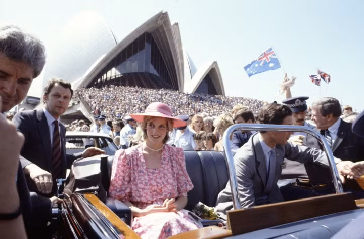 Hai vợ chồng Hoàng gia đã cùng nhau lái xe qua thủ đô Sydney, Australia, năm 1983. Công nương Diana kiều diễm trong bộ váy hoa và chiếc mũ rộng vành cùng tone màu.