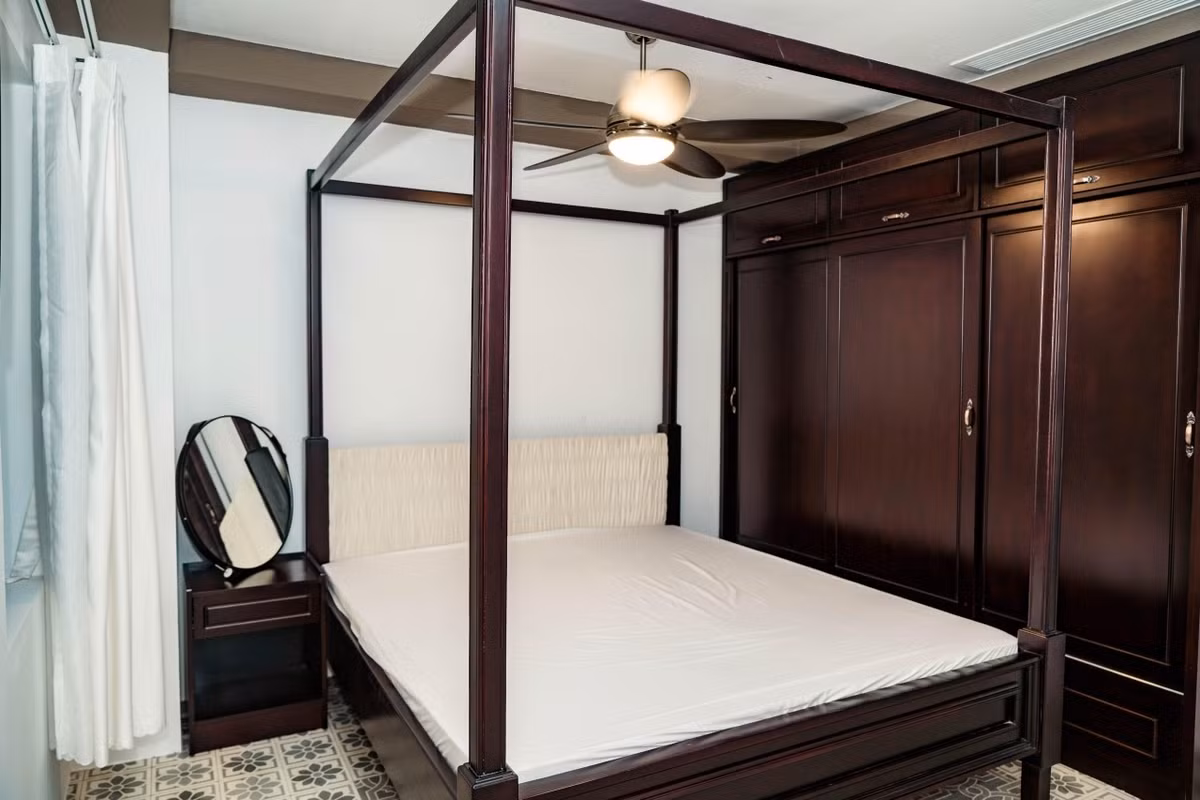 Một phòng ngủ khác mang phong cách nhiệt đới, trang trí bằng nền lót gạch hoa văn xưa và nội thất gỗ tối màu.