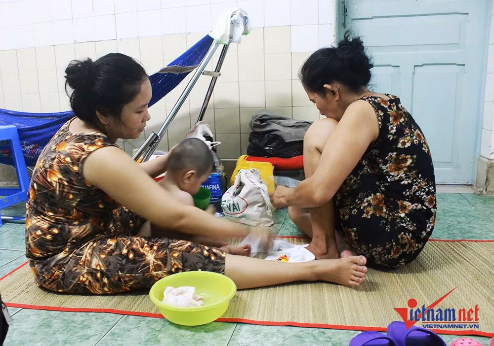 Chị Nguyễn Thị Thu Trang (Quận 2, TP.HCM) đang cho con tắm và thay quần áo. Chị cho biết, số lượng bệnh nhi đông nên mỗi giường bệnh nằm 2 bé. Ngoài ra, do thời tiết nắng nóng, chật chội nên gia đình chị phải chấp nhận mắc võng để cho con nằm ngủ ngoài hành lang.