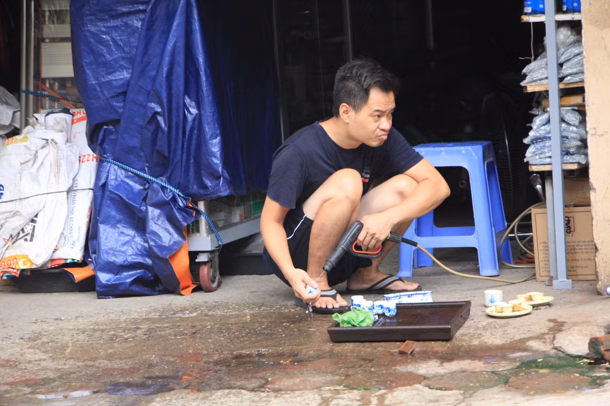 Người đàn ông mang ấm chén ra vỉa hè để cọ rửa và tranh thủ "ngắm đường".
