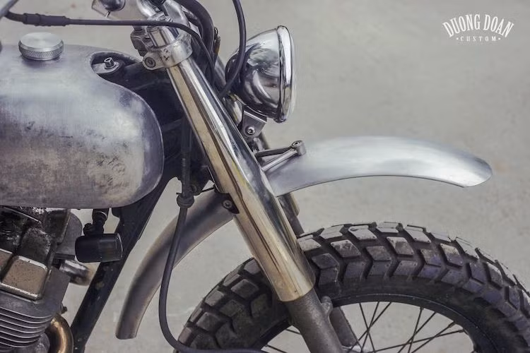 Để có thể biến Rebel từ dáng cruiser thành enduro, DuongDoan Design đã nâng hành trình phuộc trước của chiếc xe lên, trong khi vẫn sử dụng vỏ phuộc trên ngueyen bản. Phần đầu của chiếc xe được độ lại theo phong cách cổ điển tối giản với chóa đèn pha tròn, nằm dưới là chắn bùn cao ráo đúng chất "cào cào".
