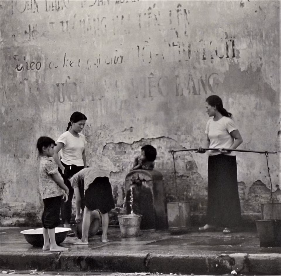 "Hà Nội 1967 - 1975" là triển lãm thứ 3 của nhiếp ảnh gia Thomas ở Việt Nam sau triển lãm năm 1972 và một buổi trình diễn cho dự án làm phim "Nước chanh đá cho Hong Li" năm 2000 trên Quảng trường Đông Kinh Nghĩa Thục ở Hà Nội. Trong ảnh là phụ nữ và các bé gái đi lấy nước để sử dụng trong sinh hoạt hàng ngày.