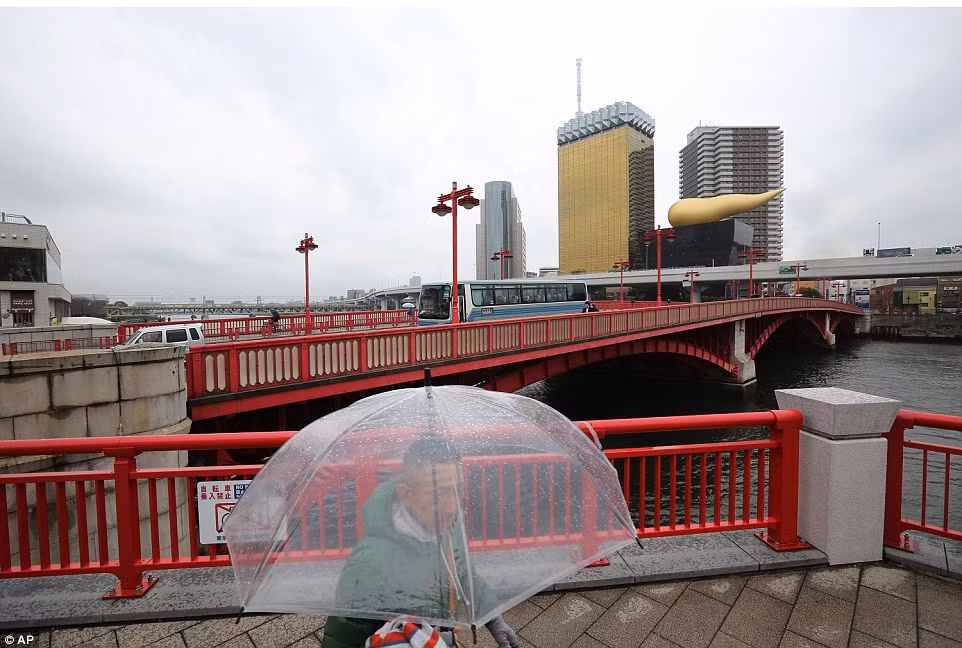 Vào lễ kỉ niệm 70 năm ngày Tokyo bị đánh bom, một người đàn ông đi bộ gần cây cầu trong khi đằng xa những tòa nhà hiện đại mọc lên tô điểm cho thành phố.