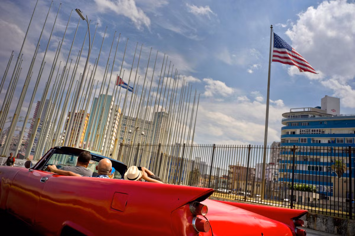 Khách du lịch ngồi trên một chiếc xe cổ đang chạy ngang qua Đại sứ quán Mỹ ở La Habana. Ảnh USN