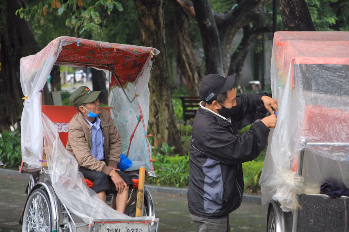 Trời mưa, gió rét nên khu vực hồ Hoàn Kiếm không có khách dạo phố nhưng những người chạy dịch vụ xích lô vẫn cố bám trụ trên đường và chống chọi mưa rét bằng cách chằng buộc áo mưa xung quanh xe.