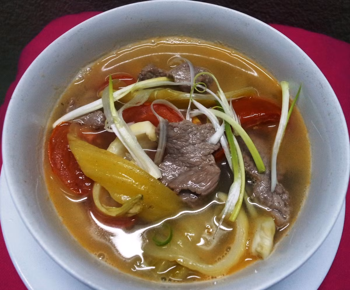Canh thịt bò dưa chua. Nguyên liệu: Thịt bò: 150 gr, dưa chua: 2 bát con, cà chua: 2 quả, hành khô, tỏi, hành hoa, rau mùi, hạt tiêu, hạt nêm, gia vị. Thực hiện: Thịt bò rửa sạch, thái miếng mỏng rồi ướp thịt với một ít hạt nêm, gia vị. Ướp khoảng chừng 15 phút thì ướp tiếp thịt bò với một ít dầu ăn để cho thịt bò được mềm. Hành, tỏi khô bằm nhỏ. Hành hoa, rau mùi cắt khúc. Cà chua bổ múi cau.