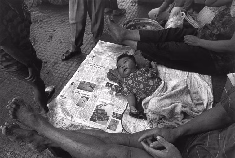 Em bé nằm trên nền gạch trải báo cũ ở một khu chợ TP HCM. Ảnh: Ferdinando Scianna/ Magnumphotos.com.