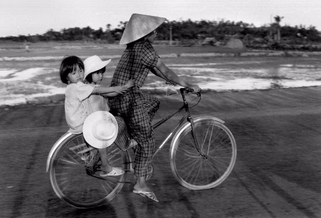 Hai bé gái sau xe đạp của mẹ ở vùng nông thôn gần TP HCM. Ảnh: Ferdinando Scianna/ Magnumphotos.com.