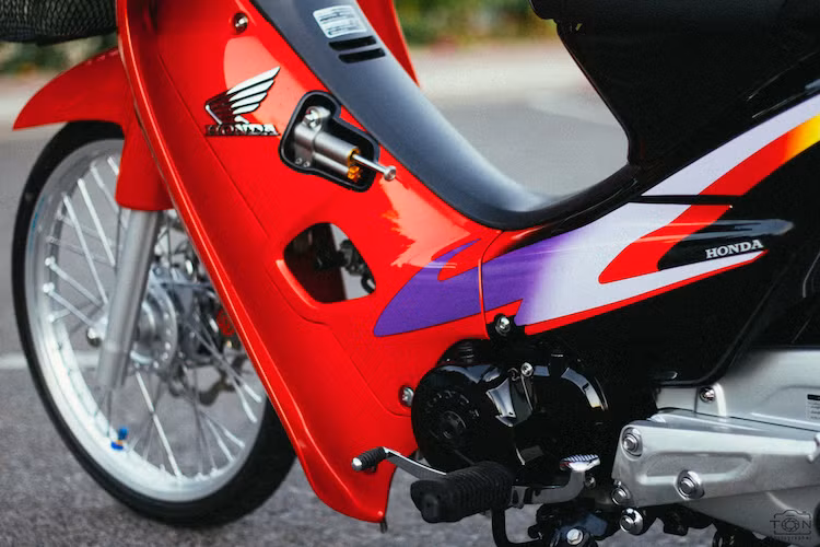 Nằm ở bên dưới yếm xe còn có một cây trợ lực Ohlins để khiến chiếc Wave ổn định hơn ở tốc độ cao. Trong khi đó, khối động cơ nguyên bản của chiếc xe hoàn toàn không có sự thay đổi, chỉ được phục chế lại về như mới. Dàn vỏ nguyên bản của xe được sơn lại trong tông màu đen-đỏ và đi tem Wave S 110.