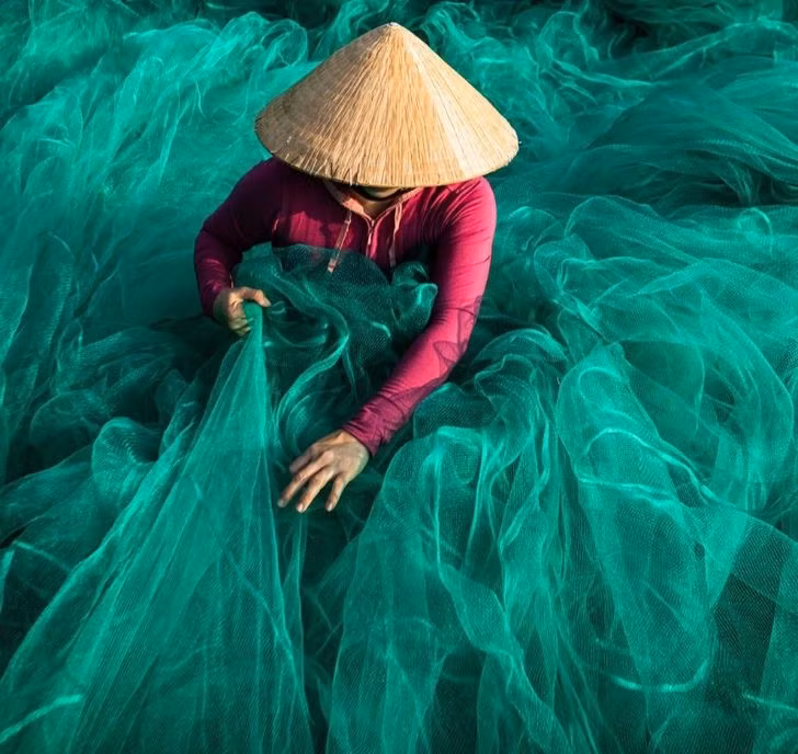 Một phụ nữ Việt Nam kiểm tra và sửa những chiếc lưới đánh bắt cá trước khi chúng được các ngư dân mang đi biển.