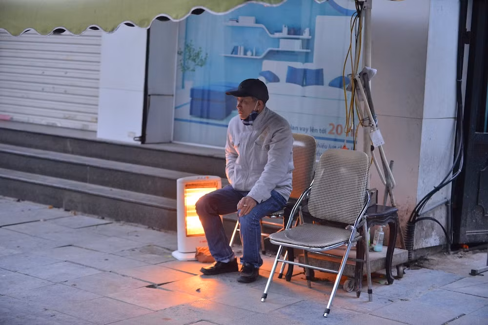 Một người dân vừa trông cửa hàng ngồi bên cạnh máy sưởi. (Ảnh: Saostar) 