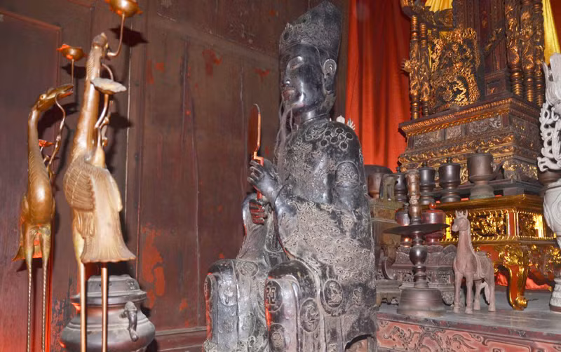 Vua đội mũ bình thiên hai cấp, trang trí "lưỡng long chầu nhật". Khuôn mặt vua vuông chữ "điền", mang phong cách của nghệ thuật tượng chân dung. Mình mặc áo long bào cổ cao, hai tay cầm hốt để trước ngực, diềm áo chảy xuống tới tận mũi hài. Thân đeo đai ngọc to bản trễ xuống, chân đi hài mũi cong.