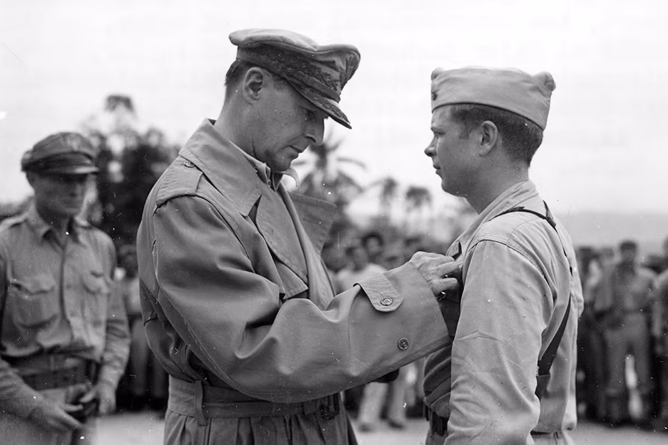 Tháng 8/1944, phi công Bong quay trở lại Phi đoàn Không quân số 49 và được giao nhiệm vụ là giáo viên bay, đồng thời tham gia chiến đấu; đến tháng 12/1944, ông đã bắn hạ thêm 14 máy bay của Không quân Nhật Bản, đưa số máy bay bị ông bắn hạ lên tới 40 chiếc. Tướng Douglas MacArthur tặng ông Huân chương Danh dự. Ảnh: Tướng Douglas MacArthur gắn Huân chương cho phi công Bong - Nguồn: Wikipedia.