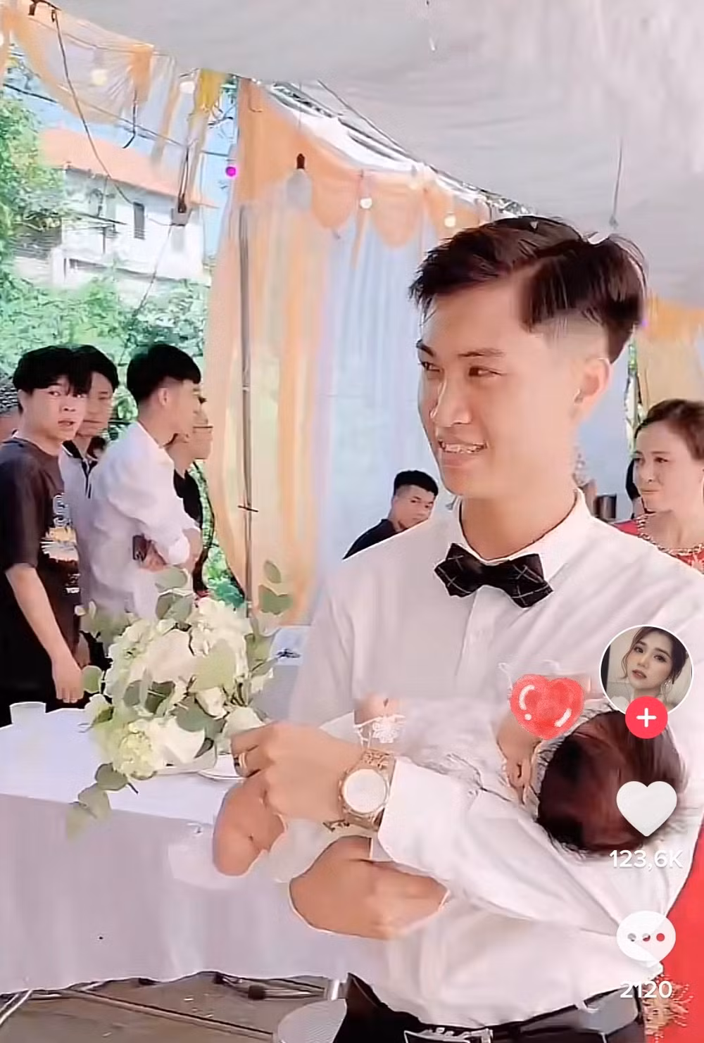 Chú rể ân cần bế một em bé khoảng vài tháng tuổi tiến vào lễ cưới. Gương mặt anh tràn ngập niềm hạnh phúc, em bé cũng nằm rất ngoan ngoãn trong lòng.