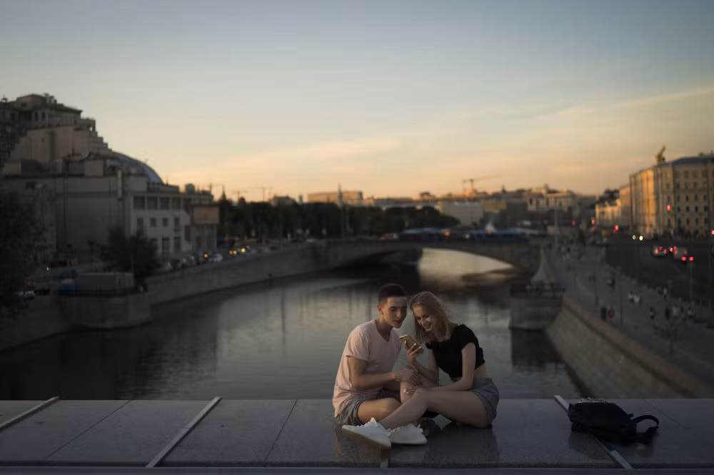 Cặp đôi ngồi xem điện thoại trên cây cầu ở thủ đô Moscow lúc hoàng hôn ngày 26/6.