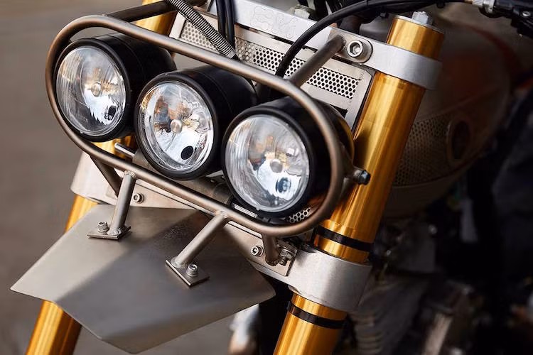 Trong khi đó, cặp phuộc USD trên bản độ là của một chiếc Yamaha WR250R đời 2014, nhưng được lắp vào chảng ba nhôm CNC do Classified Moto thiết kế để vừa với bánh lớn. Xưởng cũng không quên tạo cho chiếc xe một dàn đèn pha và chắn bùn thật "độc".