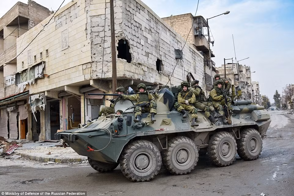 Các binh sĩ Nga ngồi trên xe tăng đi qua một con phố vắng vẻ ở Aleppo.