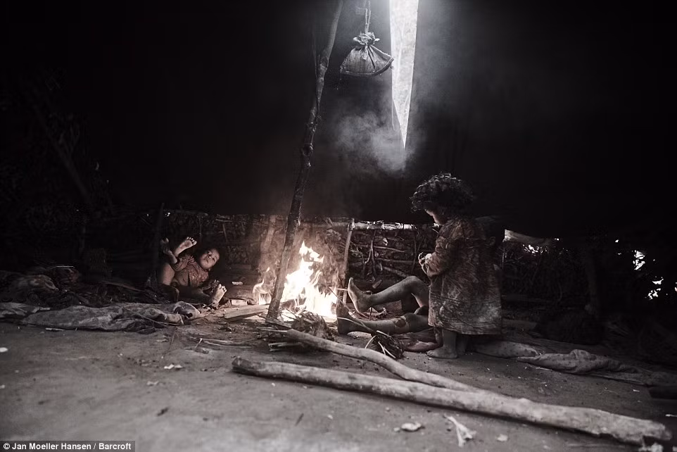 Các em nhỏ ngồi cạnh đống lửa để sưởi ấm.