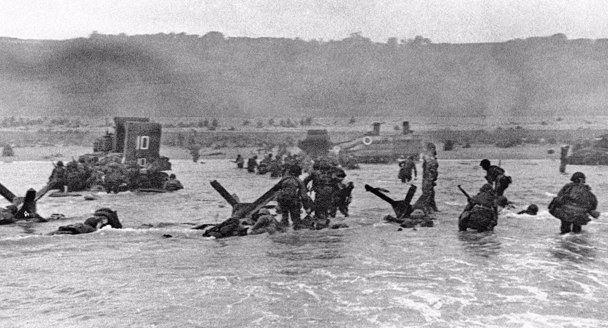 Binh lính Mỹ trong đợt tấn công đầu tiên lên lên bãi biển Normandy nấp sau những tấm chắn xe tăng đổ bộ. Trong buổi sáng ngày 6/6/1944, không một chiếc xe tăng nào của Quân Đồng Minh vào được bở biển, Không quân ném bom toàn trượt và lực lượng bộ binh phải tự chiến đấu để chọc thủng hàng phòng ngự của lính Đức. Nguồn ảnh: Theatlantíc.