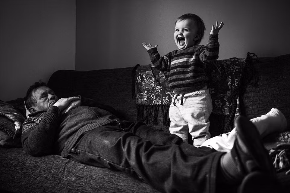 Bức ảnh “Wake Up Call” ghi lại khoảnh khắc hân hoan hiện lên khuôn mặt của bé trai trước khi cháu nhảy lên người người ông đang ngủ đã chiến thắng ở hạng mục Nụ cười. Ảnh của nhiếp ảnh gia người Scotland Alex Ingle thực hiện.