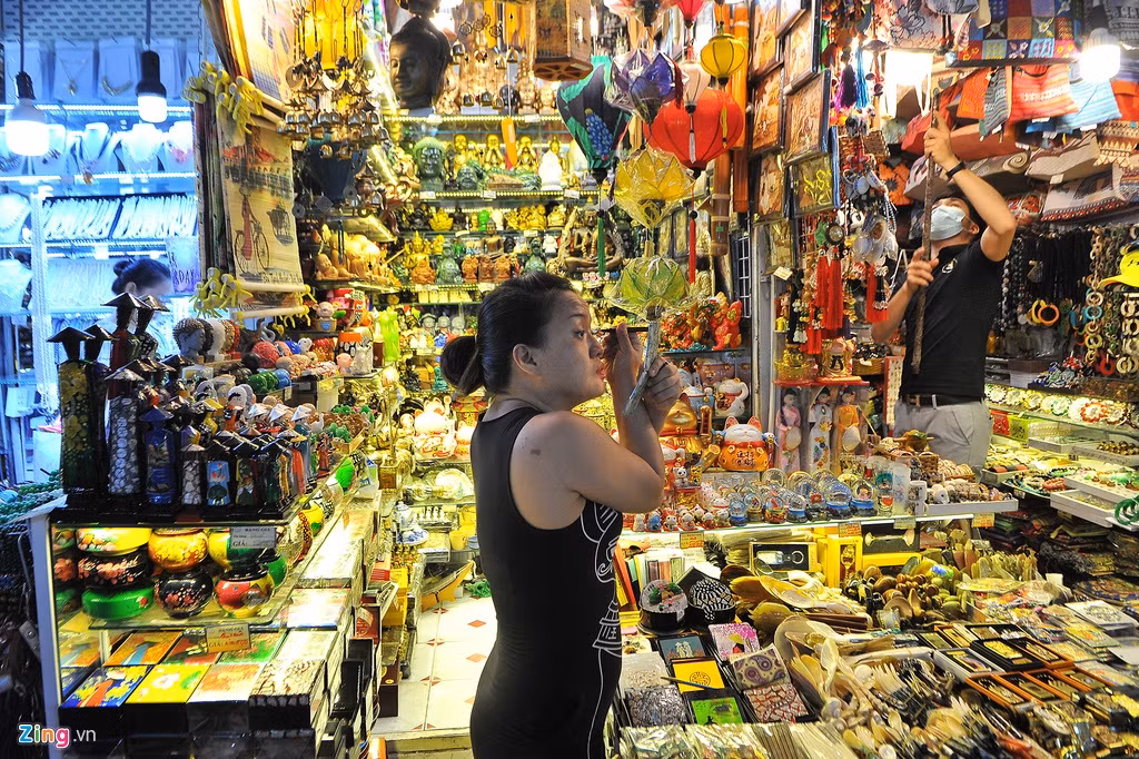Hơn 10h sáng, một tiểu thương vẫn thảnh thơi trang điểm tại sạp bán đồ mỹ nghệ của mình. Được biết lúc trưa có dịch Covid-19, thời gian này thuộc khung giờ "cao điểm" buôn bán tại chợ, hoạt động mua bán diễn ra tất bật.