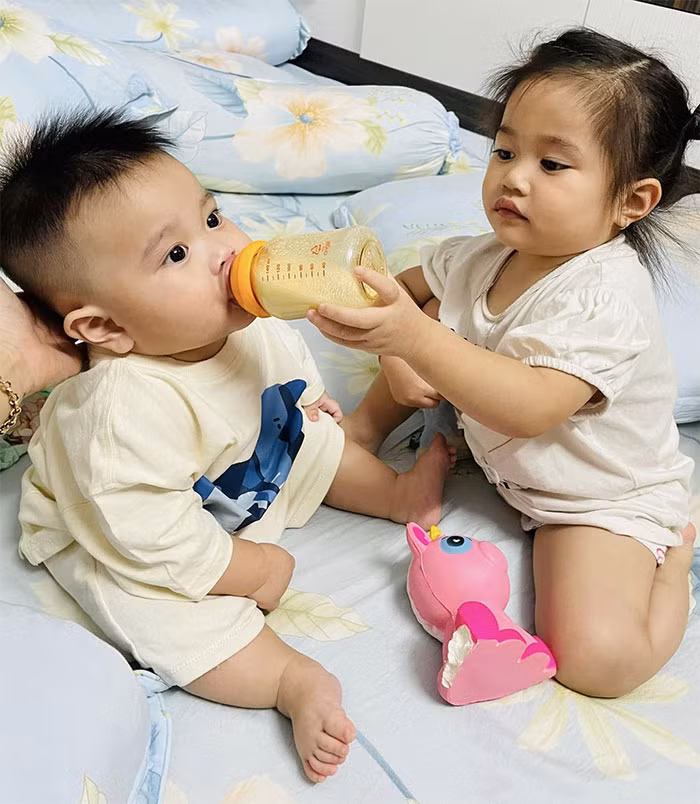 Chị Ba giúp bố mẹ cho em trai út uống sữa.