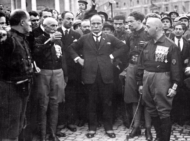 Thủ tướng Ý Benito Mussolini: Năm 1943, do những thất bại của quân đội Italia trước quân Đồng Minh, Quốc vương Italia ra lệnh truất quyền Thủ tướng và tống giam đối với Mussolini. Italia sau đó thỏa thuận với phe Đồng Minh về một giải pháp đình chiến và tuyên chiến với Đức. Tuy nhiên, người Đức vẫn cần duy trì một đồng minh như Italia và nhất là vai trò lãnh đạo của nhà độc tài Mussolini. Ảnh: Benito Mussolini tay chống hông, đứng giữa các thành viên đảng phát xít tại một cuộc diễu hành vào năm 1922.