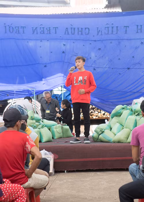 Hình ảnh Hồ Văn Cường biểu diễn ngay tại nơi trao quà với loa và âm thanh thô sơ, sân khấu chỉ là những tấm ván được ghép lên.
