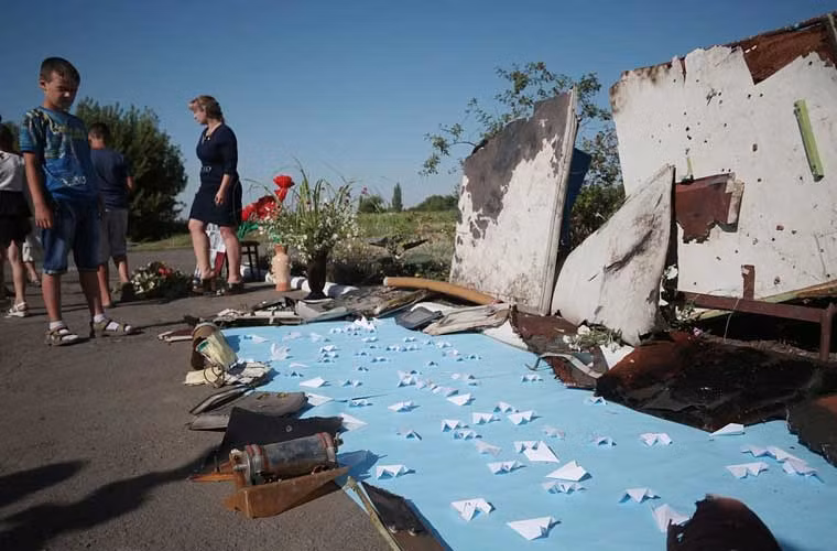 Bé trai nhìn những thứ còn sót lại của máy bay Malaysia số hiệu MH17 được đặt gần mô hình chiếc máy bay gặp nạn làm bằng giấy tại khu tưởng niệm.
