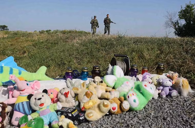 Hai dân quân thuộc phe đòi ly khai ở đông Ukraine đi ngang qua khu đất đặt gấu bông và nến tại hiện trường vụ MH17 gần làng Grabove, miền đông Ukraine.