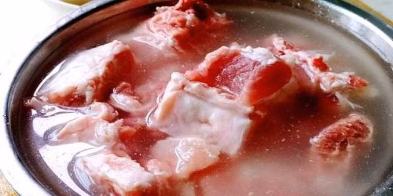 Bước 1: Sườn chặt miếng nhỏ, cho vào chậu rửa, thêm một thìa bột năng, đổ nước vào, chà mạnh tay trong 2 phút, rửa sạch sườn. Sau đó thêm nước, một thìa muối, ngâm 1 tiếng cho thấm máu. (Ảnh: Dân Việt)