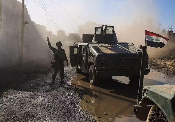 Một thành viên chính phủ Iraq giơ cao biểu tượng chiến thắng trong lúc các xe rầm rập đổ về. Ảnh FNA