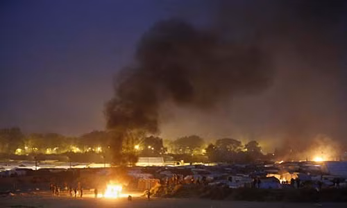 Các di dân tập trung gần đám cháy tại khu trại tị nạn Jungle ở thành phố Calais (Pháp) vào cuối ngày đầu tiên của quá trình sơ tán di dân từ khu trại này tới các trung tâm tiếp nhận người tị nạn khác ở Pháp hôm 24/10.