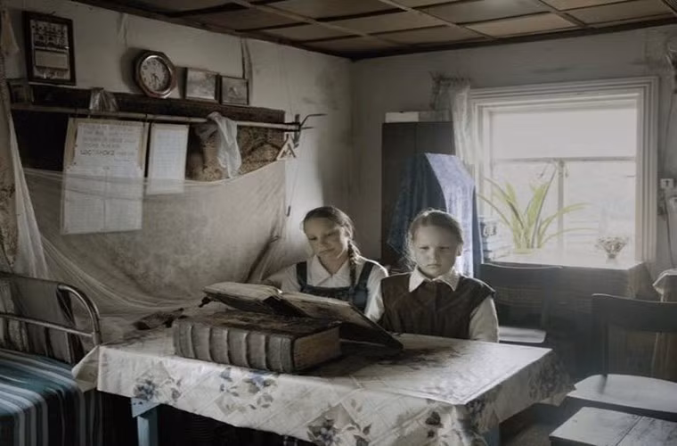 Hai em nhỏ ngồi đọc sách trong nhà ở ngôi làng nhỏ giữa rừng rậm.