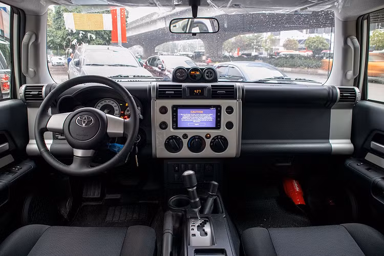 Vô-lăng trên Toyota FJ Cruiser mới là nhựa mềm, không được tích hợp bất cứ phím bấm chức năng nào, ngay sau đó là màn hình Analog dạng truyền thống với vòng tua tốc độ ở vị trí trung tâm. Mẫu SUV lai xe VAN của thương hiệu Nhật Bản cũng chỉ có chìa khoá cơ, đèn pha chỉnh tay nhưng lại có cửa kính lái auto.