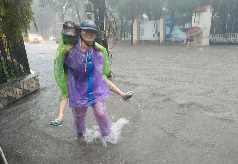 Nước ngập sâu làm em nhỏ không thể đi bộ qua được, và phải nhờ phụ huynh cõng.