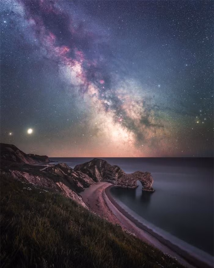 Bức ảnh dải ngân hà lấp lánh phía trên vòm đá vôi tự nhiên Durdle Door ở Lulworth, khu vực đường bờ biển nổi tiếng của Anh. Trong dải ngân hà, Sao Thổ và Sao Mộc ẩn nấp ở ngoại vi bên trái của bức ảnh. Tác giả: Anthony Sullivan. Danh sách rút gọn cho giải thưởng Nhiếp ảnh thiên văn của năm 2021 đã được Viện bảo tàng Hoàng gia Greenwich công bố. Giải thưởng hiện bước sang năm thứ 13, được coi là cuộc thi chụp ảnh thiên văn hàng đầu trên thế giới.