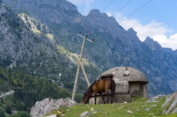 Một con ngựa gặm cỏ bên cạnh là boongke tránh bom hạt nhân bỏ hoang nằm ở đèo Valbona trên dãy núi Alps, Albania.