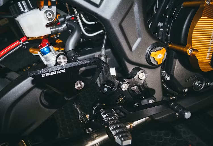 Lốc máy có thêm ốp vàng bảo vệ bằng nhôm CNC. Cả hai bên dàn để chân của xe do hãng KD Project Racing cung cấp và cũng được làm từ nhôm CNC.