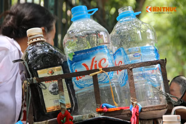 Đến khoảng 9h30, bà Thũng bắt đầu chở những chai, can nước vối mát lành trên chiếc xe máy dán 3 chữ "nước miễn phí" ra phía cổng Bệnh viện K mời mọi người uống.